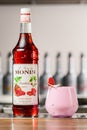 UKRAINE, KYIV - MARCH 12, 2021: bottle of raspberry syrup by Monin brand and glass of cocktail garnished with coconut