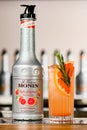 UKRAINE, KYIV - MARCH 11, 2021: Close-up of bottle of Ruby Grapefruit Syrup by Monin and glass of cocktail with citrus Royalty Free Stock Photo