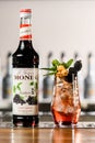 UKRAINE, KYIV - MARCH 12, 2021: Front view of bottle of Monin blackberry syrup and glass of cold signature cocktail with