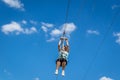 Zipline. A view of a man sliding on a steel cable against a beautiful blue sky with white clouds. Emotion of delight.