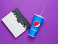 UKRAINE, ODESSA-JANUARY 7, 2019: Pepsi paper cup with straw, video cassette on purple background. Pop culture 80s, retro style Royalty Free Stock Photo