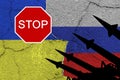Ukraine and russia flags on old cracked wall with antiaircraft rockets silhouettes and sign `STOP`
