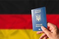 Ukrainian biometric passport in the hand of a person against the background of the national flag of Germany. Citizenship of Royalty Free Stock Photo