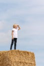 Ukrainian boy stands on haystack on blue sky background. Child leaned his palm against his eyes and looked into the distance Royalty Free Stock Photo