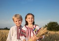 Ukrainian children boy and girl in national clothes with bouquet of dry ears of wheat are standing on field