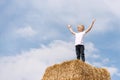 Ukrainian fair-haired stands on the haystack with his hands up against the blue sky and clouds. Weekend in the village