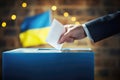 With the Ukrainian flag in the background, a man exercises his democratic right by placing a ballot into the box during