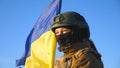 Ukrainian flag waving in wind with defocus soldier at front. Yellow-blue national symbol of Ukraine. Concept of peace