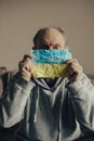 Ukrainian frightened gray haired middle aged man holds the flag of Ukraine in front of him. Po