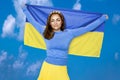 Ukrainian girl carries blue and yellow flag of Ukraine fluttering on the blue sky background. Ukrainian flag is a symbol of Royalty Free Stock Photo