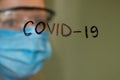 Ukrainian girl in a medical mask and glasses behind the glass on which covid-19 is written Royalty Free Stock Photo