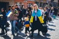 A Ukrainian refugee wrapped in a Ukrainian flag walks with a child.