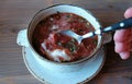 Russian national food, red beet soup, borscht. Closeup man`s hand with spoon mix sour cream in the soup.