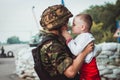 Ukrainian soldier holds child boy in his hands on roadblock against background of sandbags