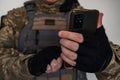 Ukrainian soldier in military pixel unform and bulletproof vest jacket with banner of flag of Ukraine holding smartphone