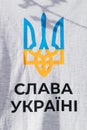 Ukrainian trident in yellow and blue inscription `Glory to Ukraine` on a T-shirt.