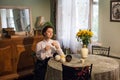 Ukrainian woman in classic clothes sits at a table with flowers, knits, in a vintage room.