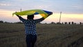 Ukrainian woman walking on barley meadow with a blue-yellow banner on shoulders at sunset. Lady going on wheat field Royalty Free Stock Photo