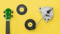 Ukulele guitar, vinyl record player and discs on a yellow background.