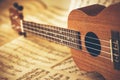 An ukulele lies on scattered sheets of paper with notes on it. Music lessons and learning solfeggio