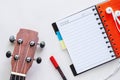 Ukulele with opened spiral notebook, pen and earphones on white Royalty Free Stock Photo