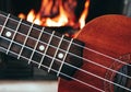 Ukulele small guitar close up stings, fireplace on the background. Musical concept, guitar fret board macro, fire in chimney, cos Royalty Free Stock Photo