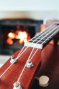 Ukulele small guitar close up stings, fireplace on the background. Musical concept, guitar fret board macro, fire in chimney, cos Royalty Free Stock Photo