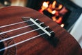 Ukulele small guitar close up stings, fireplace on the background. Musical concept, guitar fret board macro, fire in chimney, cos Royalty Free Stock Photo