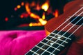 Ukulele small guitar close up stings, fireplace on the background. Musical concept, guitar fret board macro, fire in chimney, cos Royalty Free Stock Photo