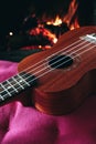 Ukulele small guitar close up stings, fireplace on the background. Musical concept, guitar fret board macro, fire in chimney, cos Royalty Free Stock Photo