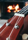 Ukulele small guitar close up stings, fireplace on the background. Musical concept, guitar fret board macro, fire in chimney, cos Royalty Free Stock Photo