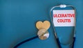 Ulcerative colitis symbol. White card with words Ulcerative colitis, beautiful blue background, wooden heart and stethoscope.