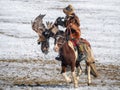 Dynamic scene of eagle training, a young hunter on a horse in motion with her golden eagle against the background of the snow-