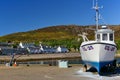 Ullapool, Scotland - May 27th, 2012 - White fishing boat ashore on the pier with harbor, waterfront buildings and mountain range i