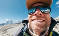 Ultra-wide lens angle portrait shot of high altitude mountain smiling unshaven happy hiker in baseball cap with snow peaks and