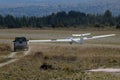 Ultralight glider plane landing with van waiting to tow it with trees in the background