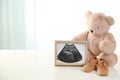 Ultrasound picture, teddy bear and baby shoes on table against light background. Royalty Free Stock Photo