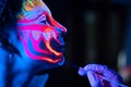 Ultraviolet black light glowing bodyart processing on young woman`s face. Pink and purple dyes in cold blue light