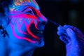 Ultraviolet black light glowing bodyart processing on young woman`s face. Pink and purple dyes in cold blue light Royalty Free Stock Photo