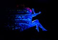 Ultraviolet black light glowing bodyart on young woman`s body. Dispersing girl on black background. Art creative concept