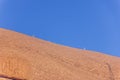 Reddish rock of Uluru or Ayers Rock with people climbing up to it`s top.