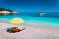 Umbrella and beach accessories on pebble beach on lazy summer day. Sailing boat stays at anchor in calm crystal clear