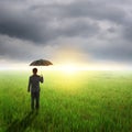 Umbrella man standing to raincloud in grassland with umbrella