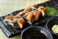 Unagi sushi on black plate along with Japanese sauce and green l