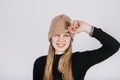 Unaltered candid emotional portrait of young happy blonde long hair woman covering eyes with brown knitted beanie hat