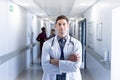 Unaltered portrait of caucasian male doctor with arms crossed, smiling in hospital corridor Royalty Free Stock Photo