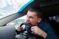 An unbalanced, goosey man bites a car steering wheel from anger while driving in a traffic jam or after an accident. A nervous and Royalty Free Stock Photo