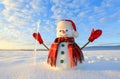 Unbelievable sunrise. Happy snowman in hat, scarf, red gloves with ice pikestaff is standing on the snow lawn. Mountains landscape