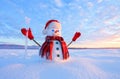 Unbelievable sunrise. Happy snowman in hat, scarf, red gloves with ice pikestaff is standing on the snow lawn.