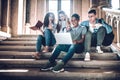 It is unbelievable! Surprised group of students looking at laptop and keeping mouth open while while sitting on the stairs in the